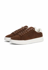 Sneaker in suede marrone con suole in gomma bianca, dotate di lacci piatti marroni e un design minimalista. Accentate da sottili dettagli di branding.