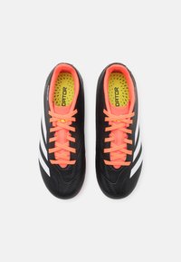 Scarpe da calcio nere con strisce bianche, lacci arancioni brillanti e superficie texturizzata. All'interno presentano una soletta gialla con perforazioni.