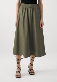 Olivegrüner Midirock mit elastischem Bund, aus leichtem Stoff. Kombiniert mit schwarzen Riemchensandalen mit Absatz.