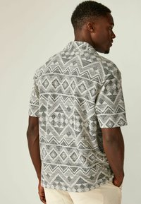 Camisa de manga corta en una tela ligera, con un patrón geométrico en blanco y negro que presenta diamantes y rayas horizontales.