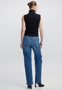 Top nero senza maniche con collo alto abbinato a jeans blu a vita alta, caratterizzati da una vestibilità rilassata, orlo sfilacciato e stivaletti neri con tacco.