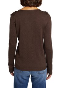 Brązowy sweter z długim rękawem, szerokim dekoltem, prążkowaną teksturą i szwami na ramionach. W połączeniu z jasnoniebieskimi dżinsami o luźnym kroju.