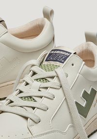 Baskets en cuir vegan blanc avec des accents en maille, des détails verts et des lacets plats. Semelle épaisse et col rembourré pour plus de confort.