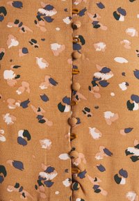 Tissu brun avec un motif tacheté multicolore et irrégulier. Comprend deux rangées de boutons au centre, avec un tissu doux et texturé.