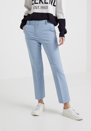 Pantaloni azzurri su misura con un taglio dritto, caratterizzati da una texture liscia e linee di piega sottili. Indossati con un maglione scuro e chiaro.
