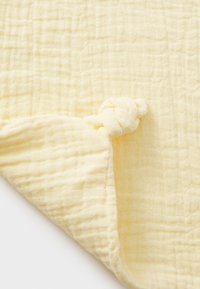 Mehek zvečer rumena bombažna odeja s teksturiranim, mrežastim vzorcem. Ima vozlane vogale za enostavno prenašanje in prijeten občutek.