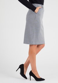 Falda lápiz de estampado pata de gallo en blanco y negro, de largo medio, con bolsillos laterales y una textura suave. Combinada con zapatos de tacón alto negros.