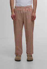 Pantaloni de pijama cu dungi în roșu și crem, cu un bandă elastică la talie și un design drept; materialul pare moale și ușor.