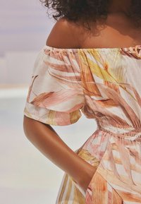 Robe florale décolletée en tissu léger avec des motifs de feuilles roses et jaunes. Taille élastique avec un détail froncé. Manches courtes bouffantes.