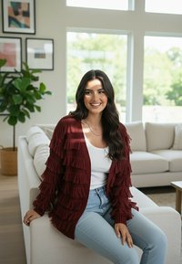 Bordowy kardigan z frędzlami o fakturowanym wzorze dzianiny, z warstwowymi falbanami, noszony na białej bluzce, w połączeniu z jasnoniebieskimi dżinsami.