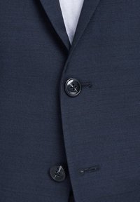 Blazer bleu marine avec une surface texturée, doté de deux boutons en plastique noir et d'un petit détail de poche. Design de revers classique.