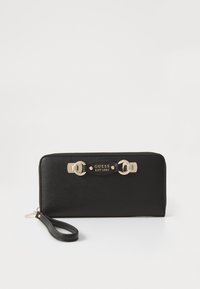 Black wallet made of textured synthetic material, featuring gold-tone hardware, a zipper closure, and a detachable wrist strap. "GUESS EST 1981" logo detail displayed.