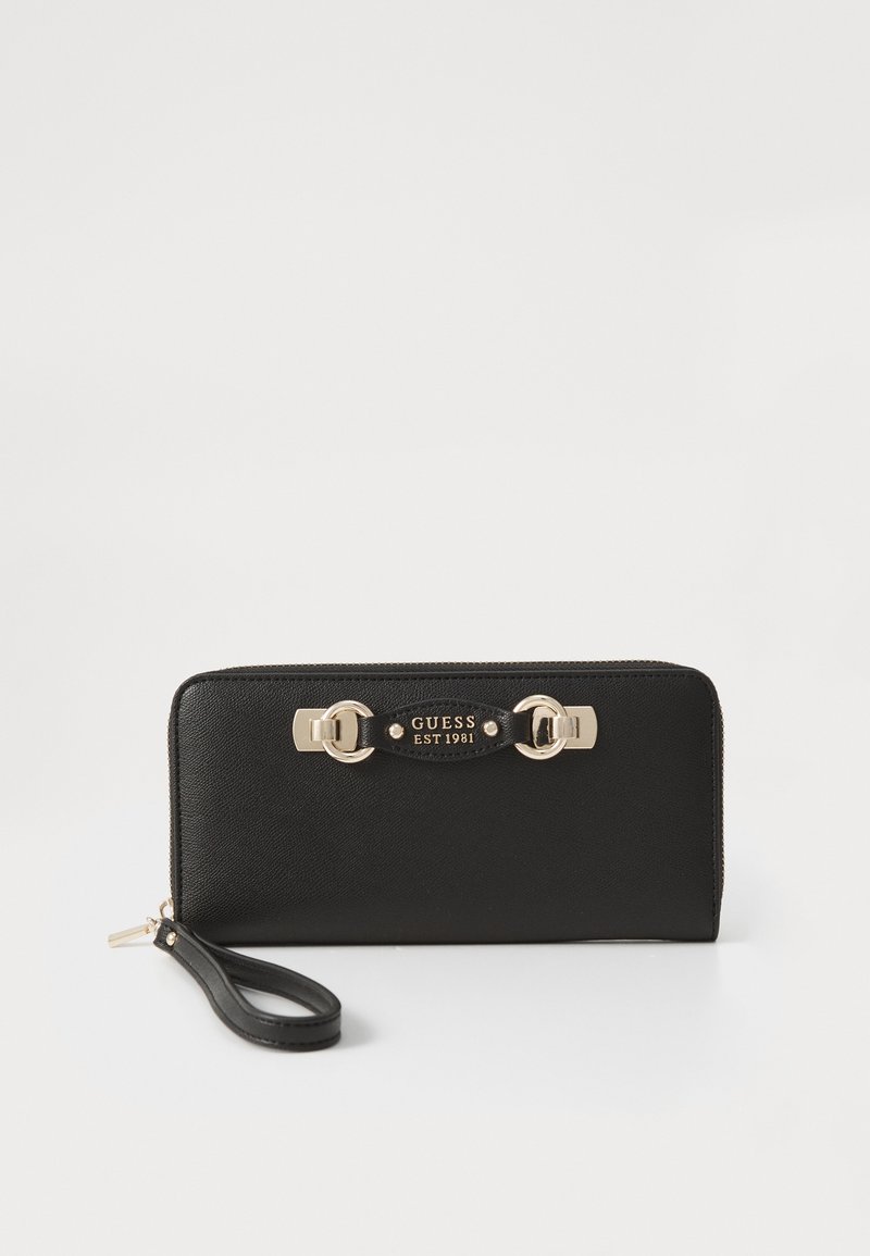 Black wallet made of textured synthetic material, featuring gold-tone hardware, a zipper closure, and a detachable wrist strap. "GUESS EST 1981" logo detail displayed.