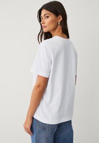 Camiseta de algodón blanca con mangas cortas, cuello redondo y corte recto. Su textura suave contrasta con unos pantalones vaqueros de mezclilla azul.