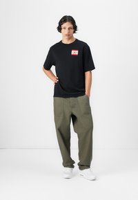 Sort bomulds t-shirt med et rødt og hvidt grafisk motiv på brystet, parret med olivengrønne baggy bukser og hvide sneakers.
