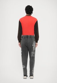 Czerwono-brązowa bluzka z długim rękawem w połączeniu z szarymi spodniami ozdobionymi białą grafiką pajęczyn i napisami, teksturowana tkanina oraz płaskie buty.