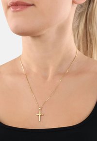Guld kors hänge halsband på en känslig kedja, med en polerad yta. Bärs mot en svart halsringning, vilket framhäver dess enkelhet och elegans.