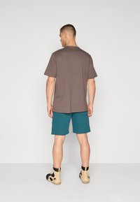 Camiseta de algodão castanha, calções teal e botas de tornozelo bege com detalhes em preto. Design simples, ajuste padrão e sem padrões visíveis.