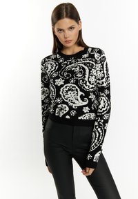 Fekete-fehér cropped pulóver, amely paisley mint�ával rendelkezik, kötött textúrájú, kerek nyakú és hosszú ujjú, fekete testre simuló nadrággal párosítva.