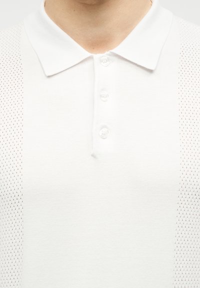 Λευκό πόλο πουκάμισο με τρία κουμπιά και πλέγμα στα πλαϊνά, φορεμένο από ένα άτομο που φαίνεται από τον λαιμό έως το στήθος.