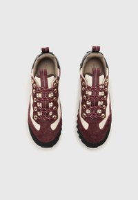 Czerwono-brązowe i kremowe buty hikingowe z zamszową i tekstylną górą, złotymi oczkami i czarną gumową sole. Charakteryzują się wyróżniającym się sznurowaniem i pętelką do zakładania.