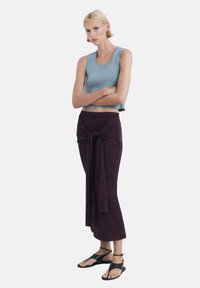 Světle modrý bezrukávový top ve spojení s dlouhou tmavě fialovou sukní s uzlem v pase. Celý outfit doplňují černé sandály na tenkých páscích.