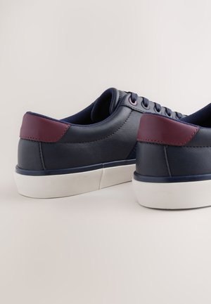 Marineblaue Ledersneaker mit burgunderroten Akzenten, abgerundeter Zehenpartie, flacher weißer Gummisohle und kontrastierendem Stofffutter. Sauberes Design.