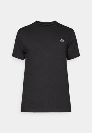 T-shirt en coton noir avec un col rond. Présente un petit logo crocodile vert sur la poitrine gauche. Manches courtes et coupe standard.