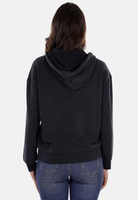 Felpa nera con tasca a marsupio, vestibilità rilassata, maniche lunghe e cappuccio. Tessuto morbido con polsini e vita a coste.