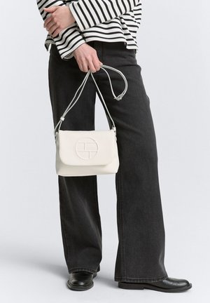 Sac bandoulière blanc avec un devant texturé et arrondi et un logo circulaire. Associé à un pantalon noir à jambes larges et un haut à rayures noir et blanc.