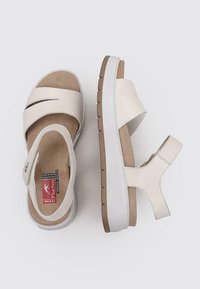 Sandalias de cuero blanco con tiras cruzadas, plantilla acolchada y una suela de goma marrón resistente con una superficie texturizada.
