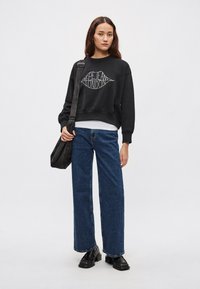 Μαύρο φανελάκι με λευκή εκτύπωση "Pepe Jeans London", σε συνδυασμό με τζιν μπλε παντελόνι wide-leg με ψηλή μέση. Το μοντέλο κρατάει μια σκούρα τσάντα ώμου.