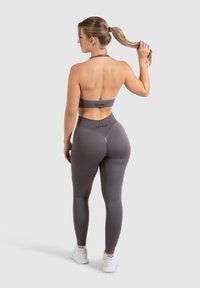 Grijze sportset met een haltertop en hoge taille legging. Het materiaal lijkt glad en heeft een aansluitend ontwerp, wat comfort en ondersteuning verbetert.
