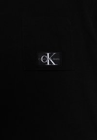 Czarny bawełniany t-shirt z kieszonką na piersi z prostokątnym logo Calvin Klein Jeans w białym haftem. Gładka faktura, prosty design.