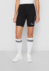 Person som bär svarta cykelshorts med vit text på sidan, vita knästrumpor med svarta ränder och vita sneakers.