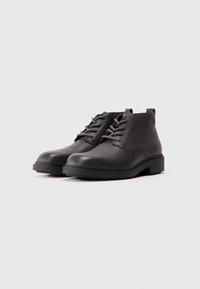 Botine negre din piele cu o suprafață texturată, design cu șireturi și o talpă robustă din cauciuc. Include un tab pentru a fi purtate cu ușurință.