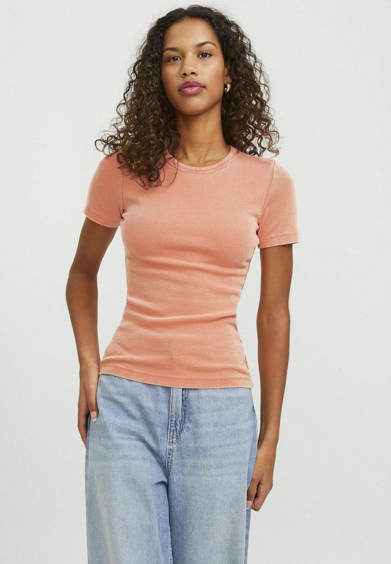 Maglietta a maniche corte a coste color pesco con scollo tondo, forma aderente e texture sottile, accoppiata con jeans a gamba larga azzurri.