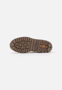 Semelle de chaussure en caoutchouc marron avec un motif de bande de roulement texturé, présentant des crampons arrondis et un logo circulaire avec des accents orange et vert.