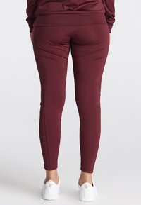 Bordeaux leggings lavet af strækbart materiale, tætsiddende design med glat tekstur, smalle ben, båret med hvide sneakers og ankellængde.
