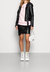 Chaqueta de motorista de cuero negro sobre un sudadera rosa, combinada con una falda de cuero negra con volantes y zapatillas altas blancas. Bolso blanco con cadena.