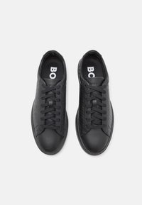 Baskets noires avec une tige en cuir texturé, un bout en caoutchouc mat lisse et des lacets noirs. La semelle intérieure porte l'inscription "BOSS" en blanc.