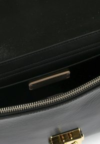 Borsa in pelle nera con cerniera e accessori in oro. L'interno mostra una fodera morbida e un'etichetta del marchio, evidenziando un design elegante e l'artigianato di qualità.