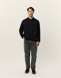 Μαύρο σακάκι με κουμπιά, με δύο τσέπες στα στήθη, σε συνδυασμό με γκρίζα τζιν και μαύρα παπούτσια. Το ύφασμα φαίνεται λείο και χωρίς υφή.