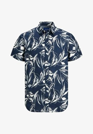 Person iført en mørkeblå blomsterprintet kortærmet skjorte, opkørte blå denimshorts, hvide sokker og hvide sneakers med mørkeblå og røde detaljer.