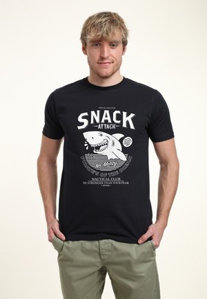 Camiseta de algodón negra con un gráfico blanco de un tiburón y un texto en negrita que dice "ATAQUE DE SNACK" con detalles náuticos y rayas.