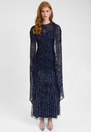 Navyblaues Abendkleid mit langen, durchsichtigen Ärmeln, bestickten Details und Perlen. Verfügt über einen gestreiften Saum und passende, verzierte Schuhe.