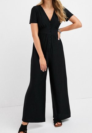 Czarny kombinezon z krótkimi rękawami, dekoltem w kształcie litery V i zapięciem na guziki z przodu. Posiada dopasowaną talię oraz szerokie spodnie, wykonany z miękkiego, elastycznego materiału.
