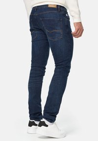 Smaltsiddende denimjeans i mørkeblå med diskret falming, der har baglommer med chevron-syning og en mærkevare-læderlap på linningen.