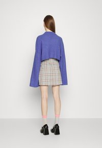 Pull violet court avec manches cloche, associé à une mini-jupe à carreaux. Le modèle porte des chaussures à talons blocs noires et des chaussettes pastel.