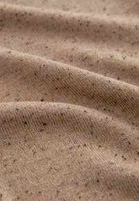 Tissu beige avec une texture douce, présentant un motif tacheté de petites fleuves noires tout au long. Le matériau semble tricoté et légèrement froissé.